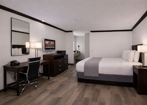 A hotel room with a bed, desk, chair, TV, and a mirror.