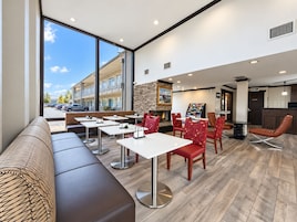 A modern outdoor seating area with tables and chairs, a stone fireplace, and a view of a parking lot and buildings.