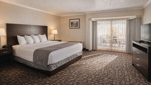 A hotel room with a large bed, two bedside tables with lamps, a television, a large window with curtains, and a patterned carpet. - Discovery Inn (Midvale)