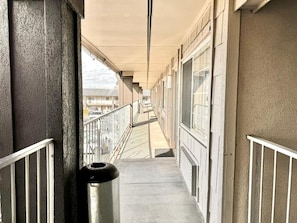 A corridor with a trash bin, metal railings, and a view of the street.