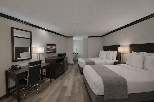 A hotel room with two beds, a desk, a TV, and a mirror. - Discovery Inn (Midvale)