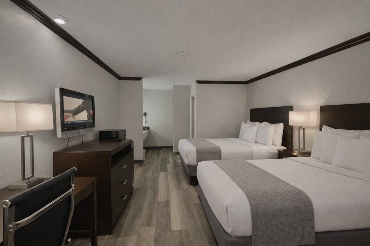 A hotel room with two beds, a desk, a television, and a chair.