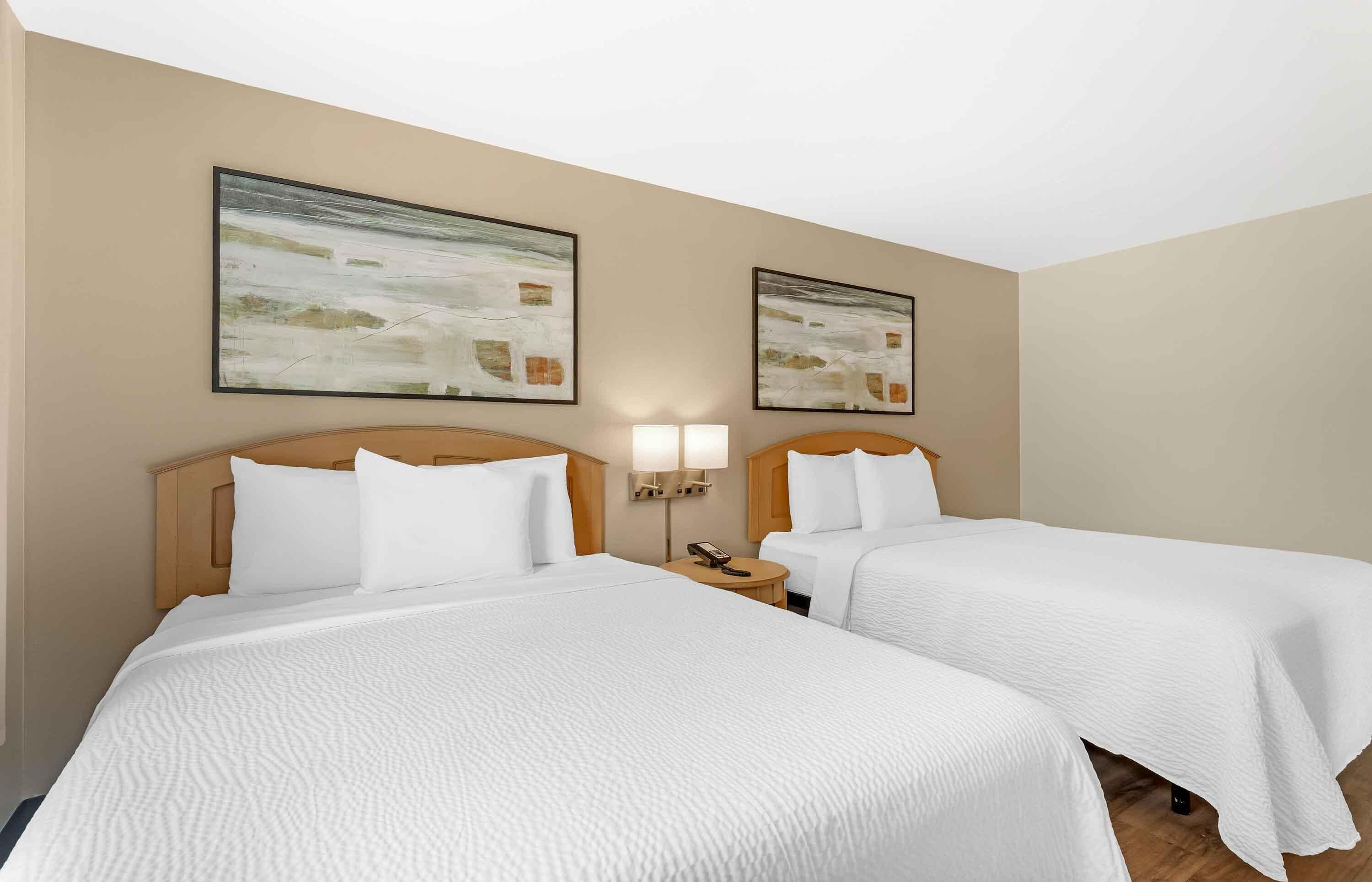 A hotel room with two beds, beige walls, and abstract paintings.