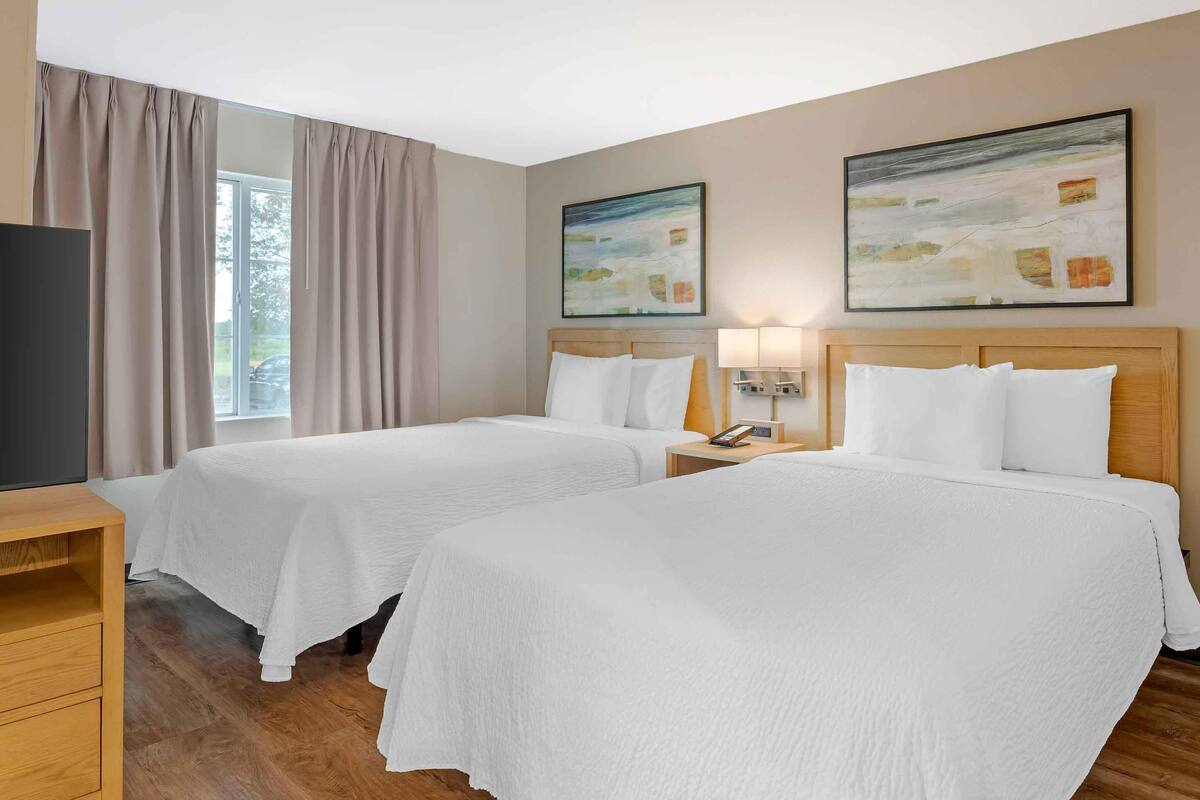 A hotel room with two beds, a TV, a desk, and artwork on the walls.