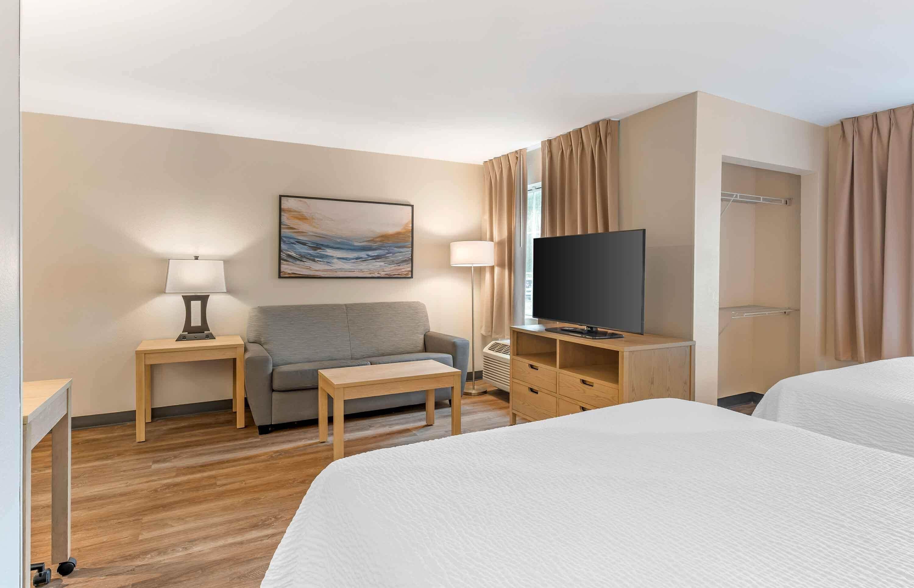 A hotel room with a bed, a sofa, a TV, a desk, and a lamp.