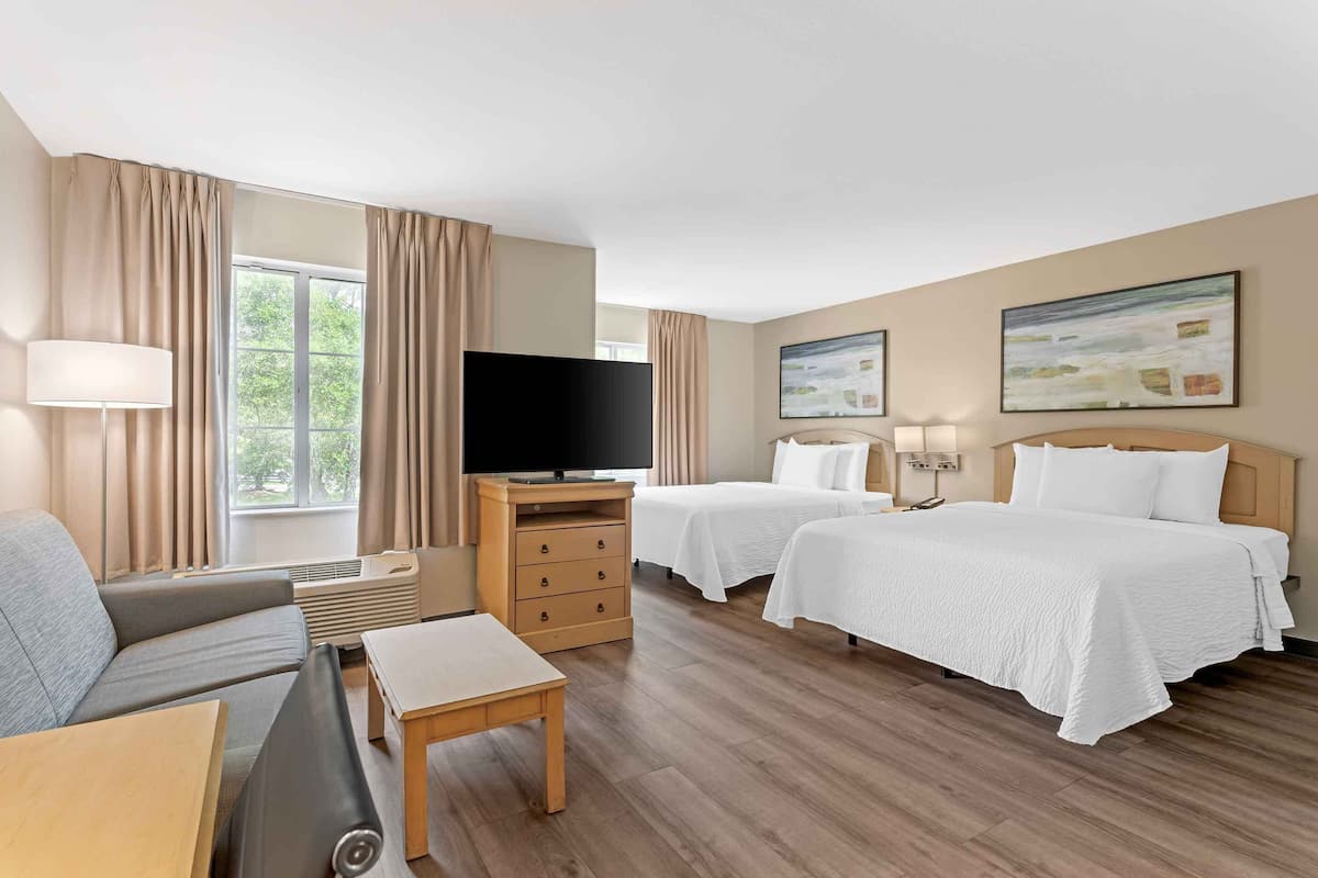 A hotel room with a sofa, two beds, a TV, a desk, and a lamp.