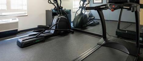 A gym with treadmills, elliptical machines, and a mirrored wall.