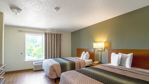 Una habitación de hotel con dos camas, un ventanal con cortinas, una lámpara de noche y un teléfono en la mesita de noche.