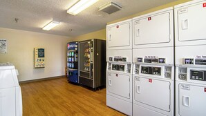 A laundry room with multiple washing machines, a vending machine, and a sign indicating hotel responsibility for items left in the room. - HomeTowne Studios by Red Roof Chicago - Waukegan (Waukegan)