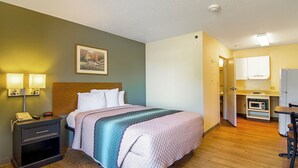 Habitación de hotel con cama, lámparas de noche, teléfono, un cuadro en la pared y una kitchenette con microondas.