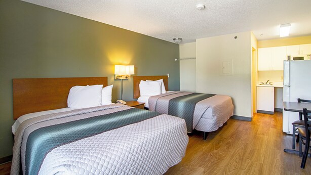A hotel room with two beds, a desk, and a kitchenette. - HomeTowne Studios by Red Roof Chicago - Waukegan (Waukegan)