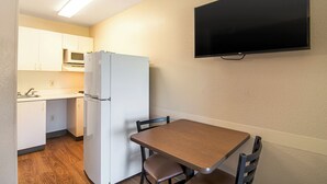 A compact kitchen with a refrigerator, microwave, and sink. A flat-screen TV is mounted on the wall above a wooden table with two chairs. - HomeTowne Studios by Red Roof Chicago - Waukegan (Waukegan)