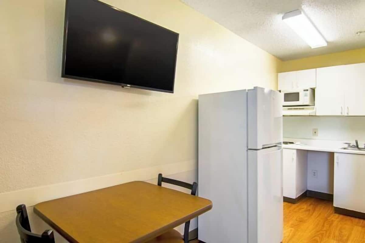 Cocina compacta con refrigerador, microondas y una pequeña mesa de comedor con una silla.
