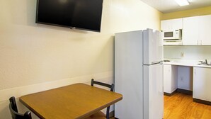 A compact kitchenette with a refrigerator, microwave, and a small dining area with a table and chair. - HomeTowne Studios by Red Roof Chicago - Waukegan (Waukegan)