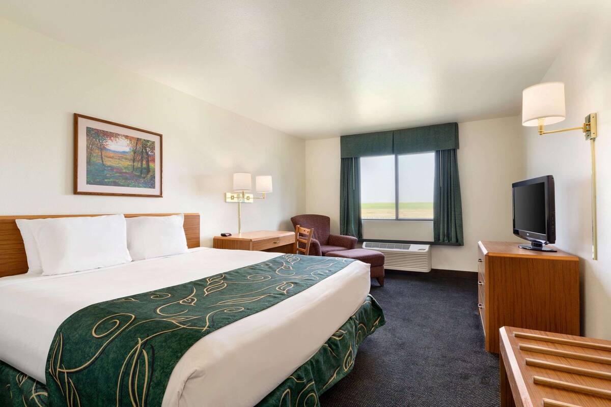 Een hotelkamer met een groot bed, een bureau met een computer, een stoel, een televisie en een raam met gordijnen.