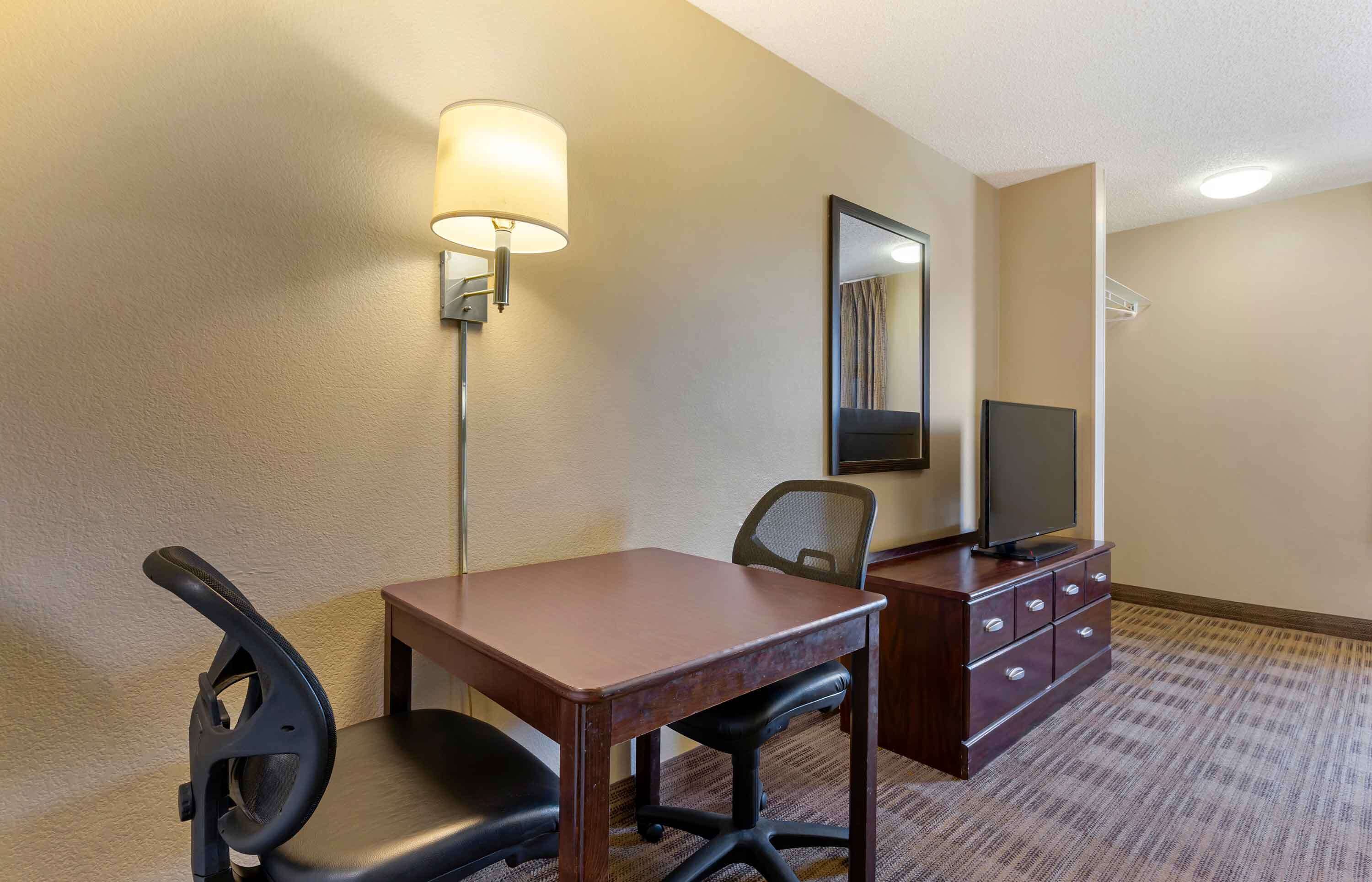 Habitación de hotel con escritorio, silla, televisor y lámpara.