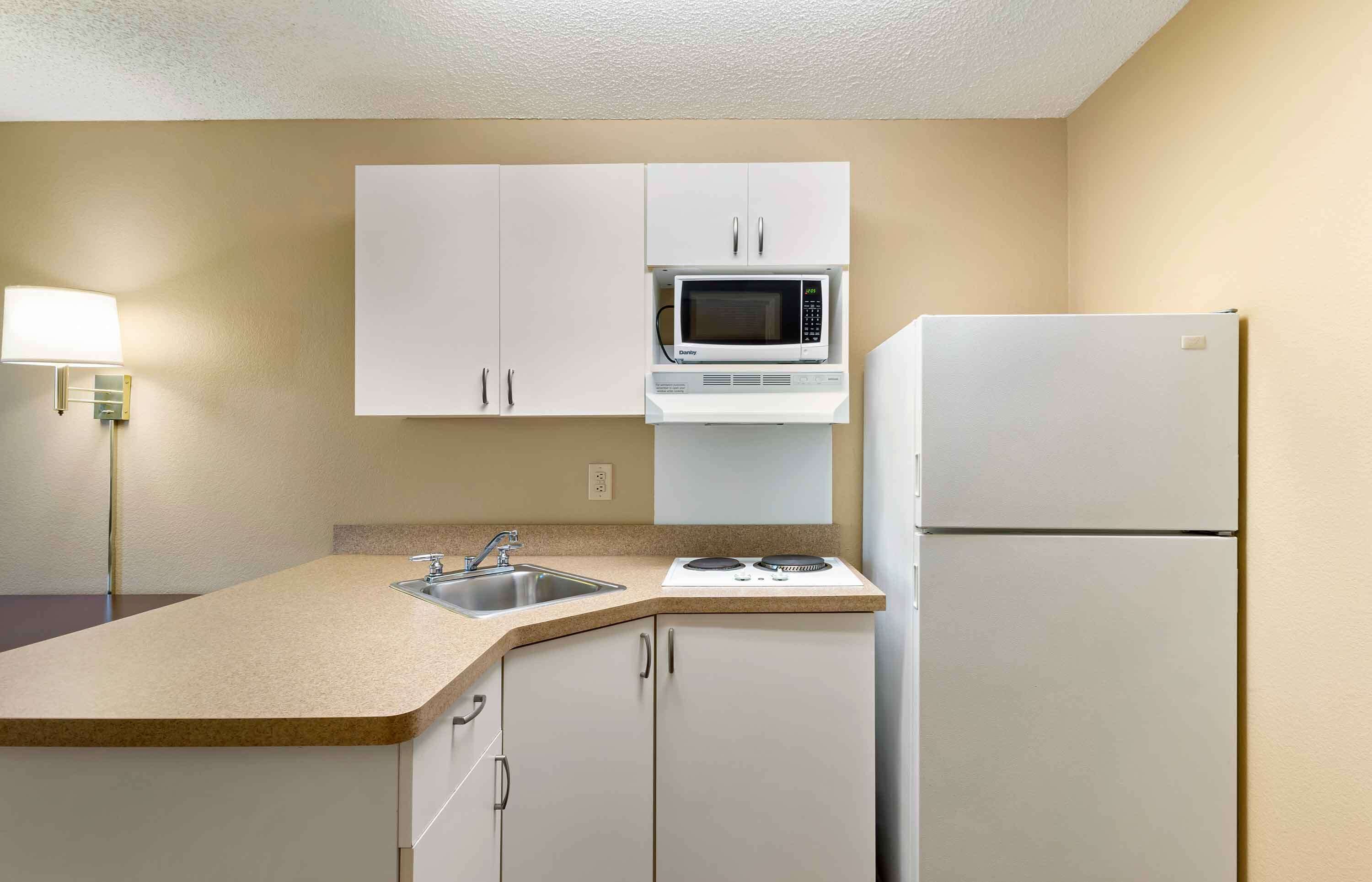 A compact kitchen with white cabinets, a microwave, a refrigerator, and a sink.