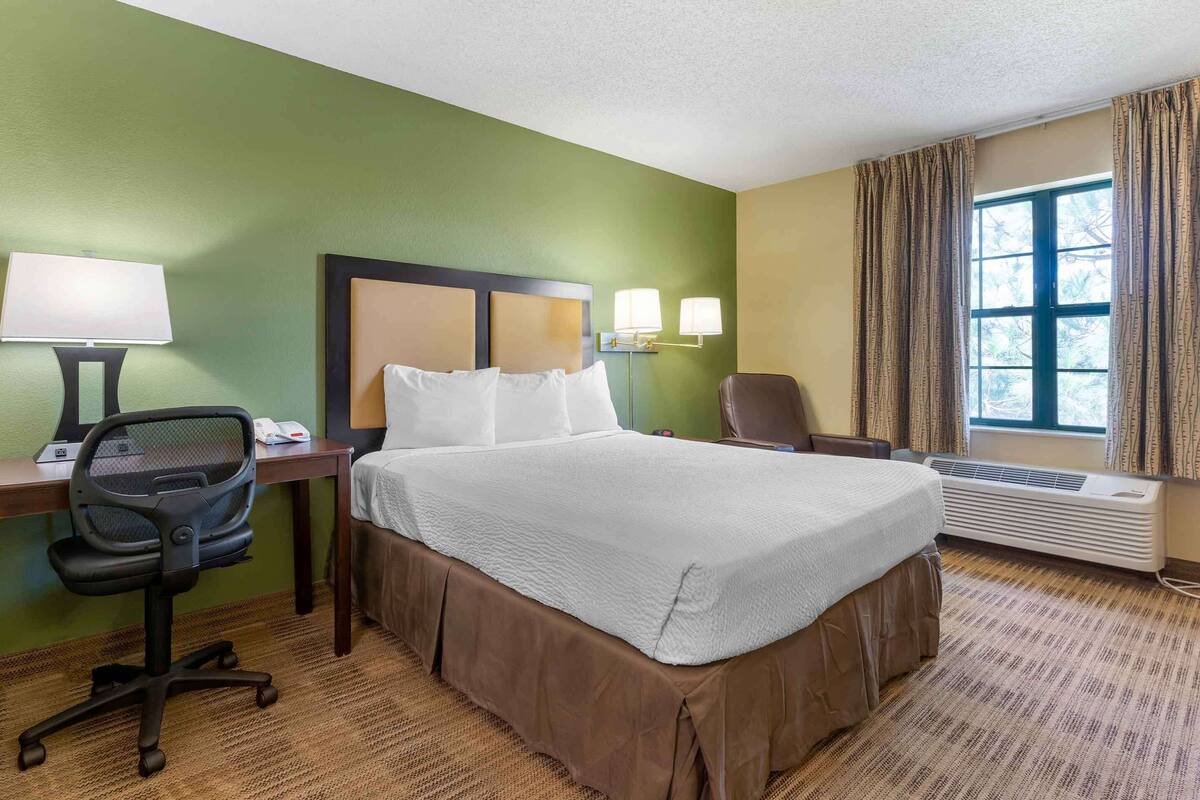 A hotel room with a bed, desk, chair, and a window with curtains.