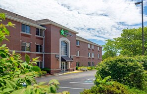 A StayAmerica hotel with a brick facade, a lobby entrance, and a parking lot. - Extended Stay America Suites Boston Woburn (Woburn)