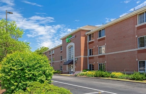 A brick building with a green logo, a clear sky, and a well-maintained garden.