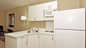 A compact kitchen with white cabinets, a microwave, a refrigerator, and a sink. - Suburban Studios Minneapolis Bloomington (Bloomington)