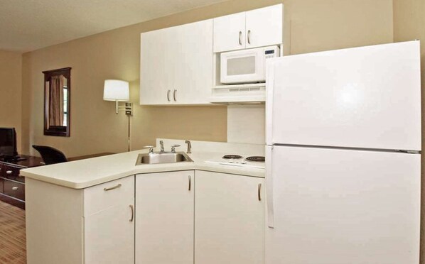 A compact kitchen with white cabinets, a microwave, a refrigerator, and a sink.