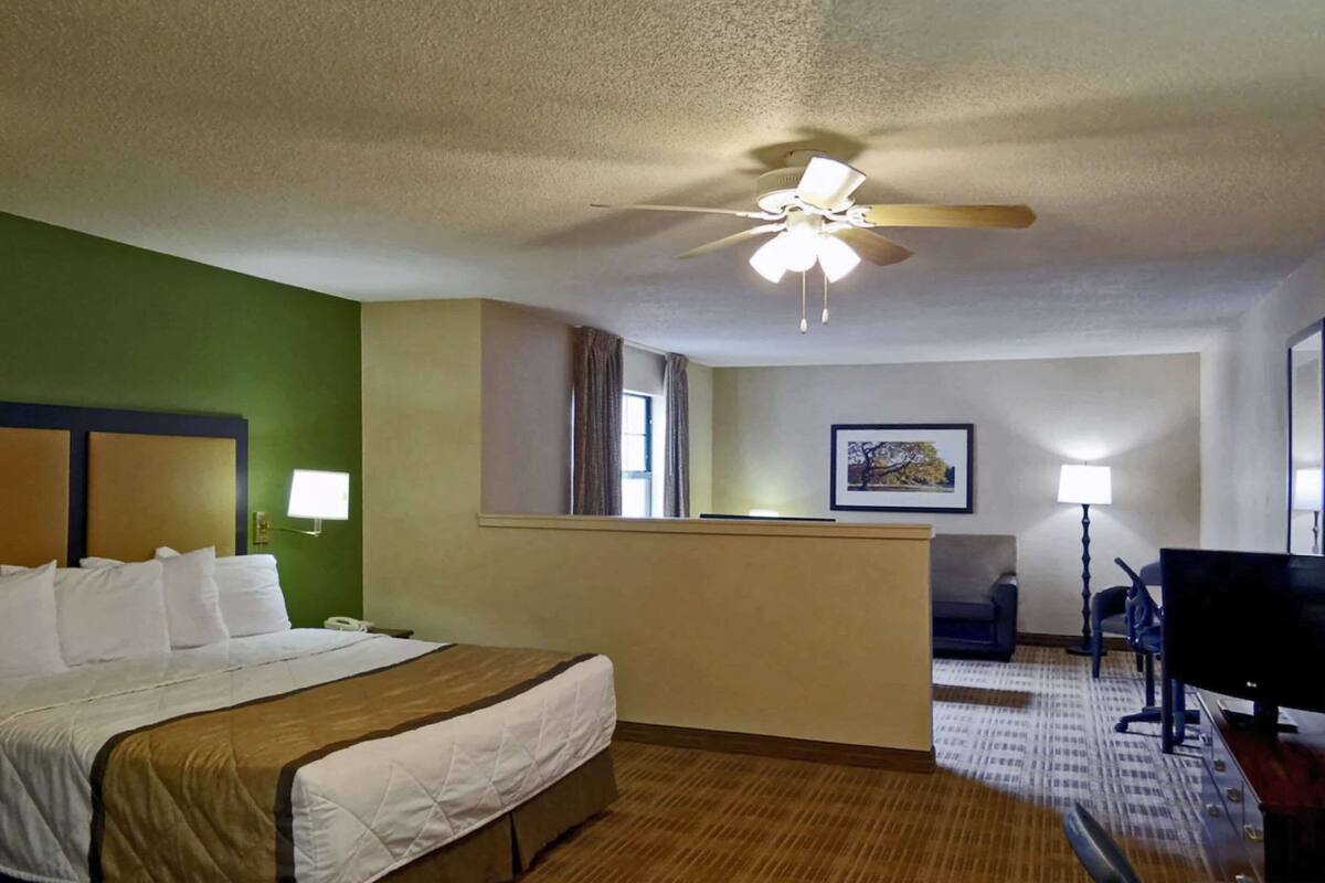 A hotel room with a bed, a desk, a television, and a ceiling fan.