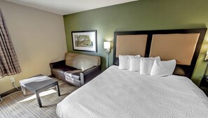 A hotel room with a large bed, a sofa, a small table, and a painting on the wall. - Suburban Studios Minneapolis Bloomington (Bloomington)