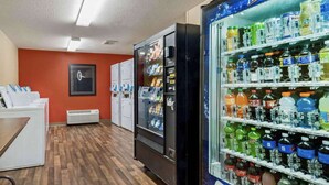 A hotel room with a wooden floor, a refrigerator with beverages, a vending machine, and a laundry area. - Suburban Studios Minneapolis Bloomington (Bloomington)