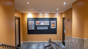A hallway with a marble floor, a wooden handrail, and three framed artworks on the wall. - The Belvedere Hotel (New York)
