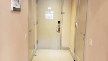 A hallway with beige walls and a tiled floor, leading to a door with a fire alarm and an evacuation plan sign.