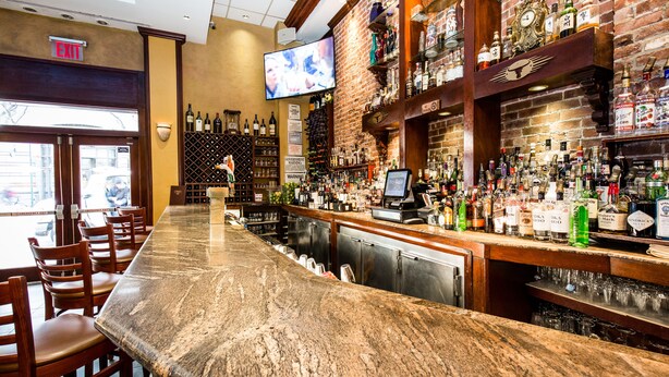 A bar with a long counter, wooden chairs, and a television mounted on the wall. - The Belvedere Hotel (New York)