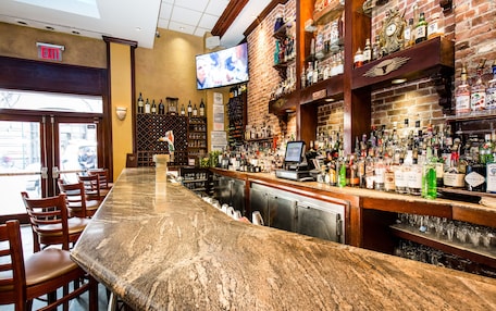 Un bar con una barra larga, sillas de madera y un televisor montado en la pared.
