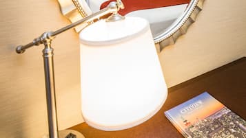 Habitación de hotel con un espejo grande, una cama con ropa de cama blanca, un cojín rojo, una lámpara de noche y dos cuadros en la pared.