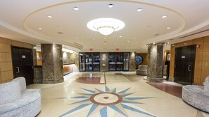 A lobby with a central sunburst design on the floor, two elevators, and a reception desk. - The Belvedere Hotel (New York)