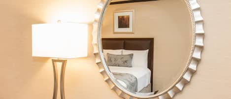 Habitación de hotel con escritorio de madera, lámpara, teléfono y espejo en la pared.