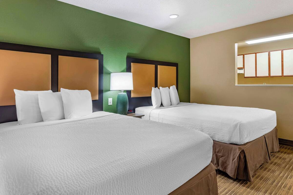 Una habitación de hotel con dos camas, una pared verde y un ventanal grande.