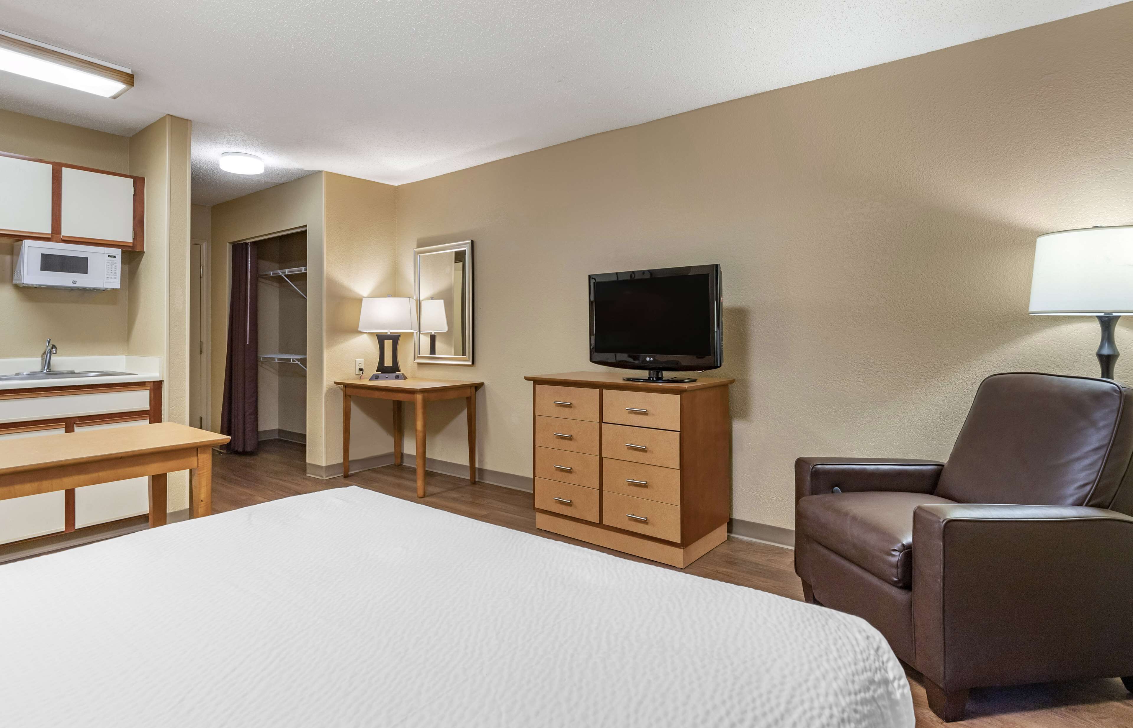 Quarto de hotel com cama, escrivaninha, televisão, cadeira, cômoda, espelho, luminária e micro-ondas.