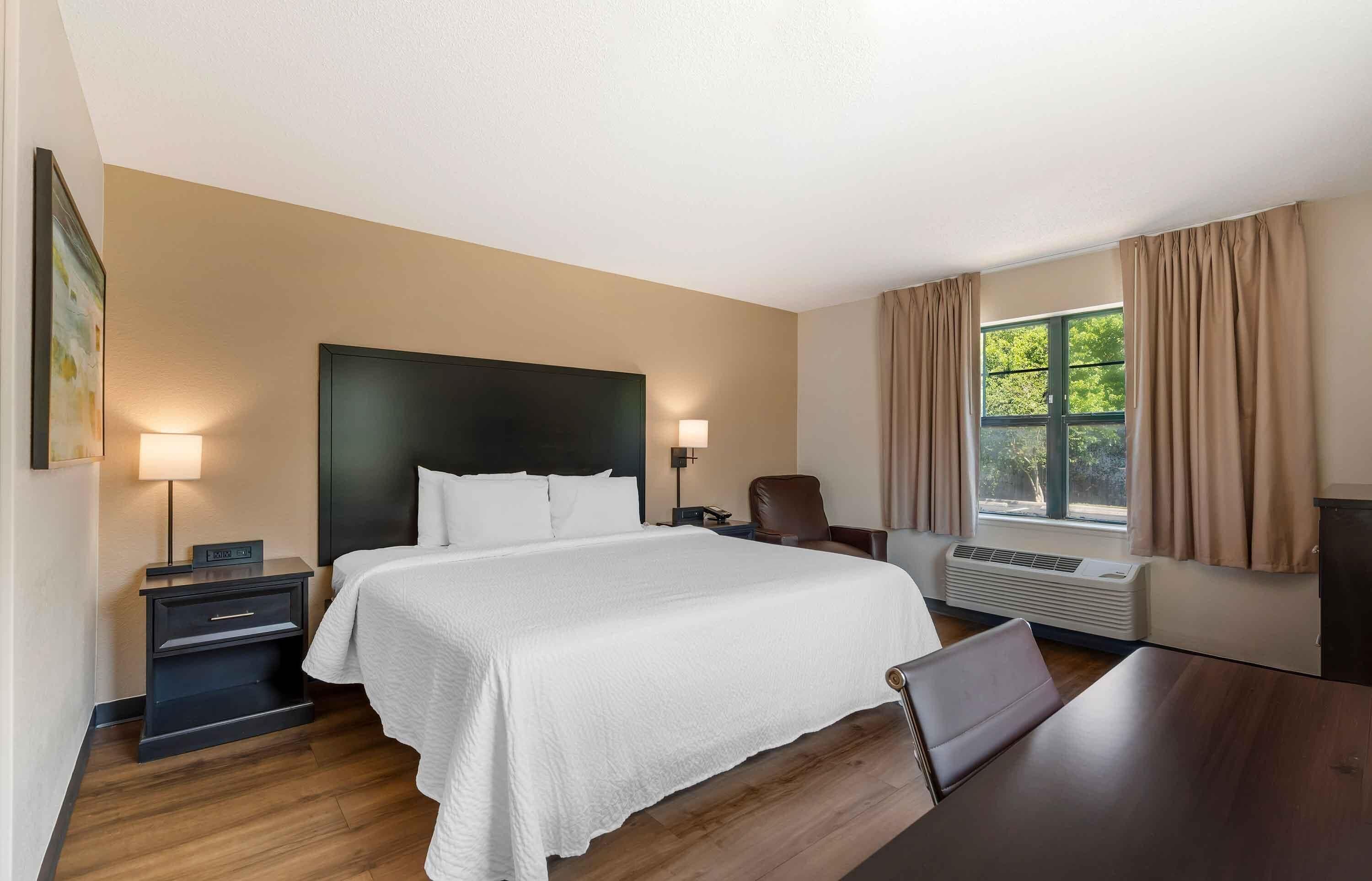 A hotel room with a bed, bedside tables, a desk, a chair, a TV, and a window with curtains.