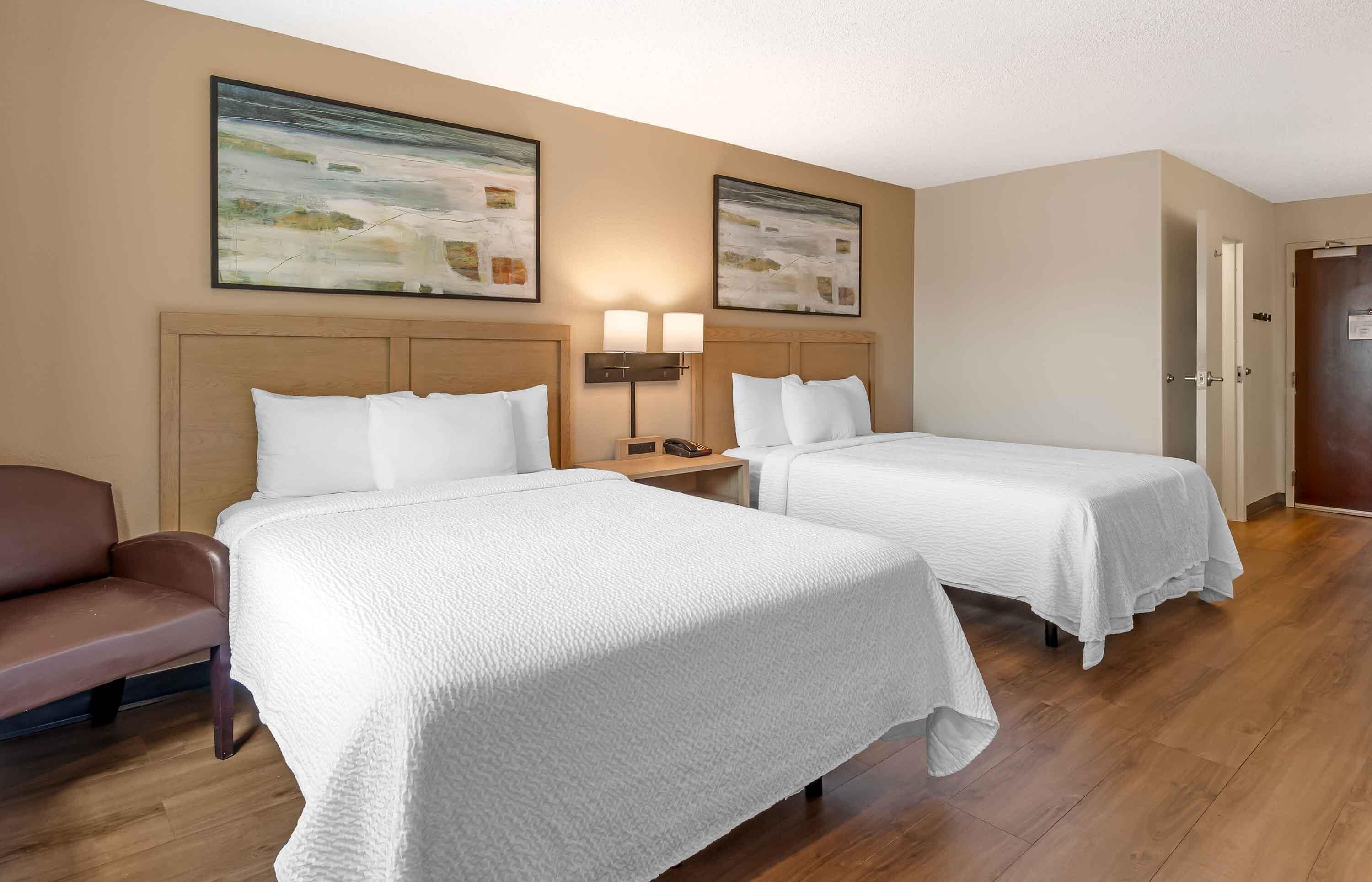 A hotel room with two beds, a sofa, a nightstand with a lamp, and two framed pictures on the wall.