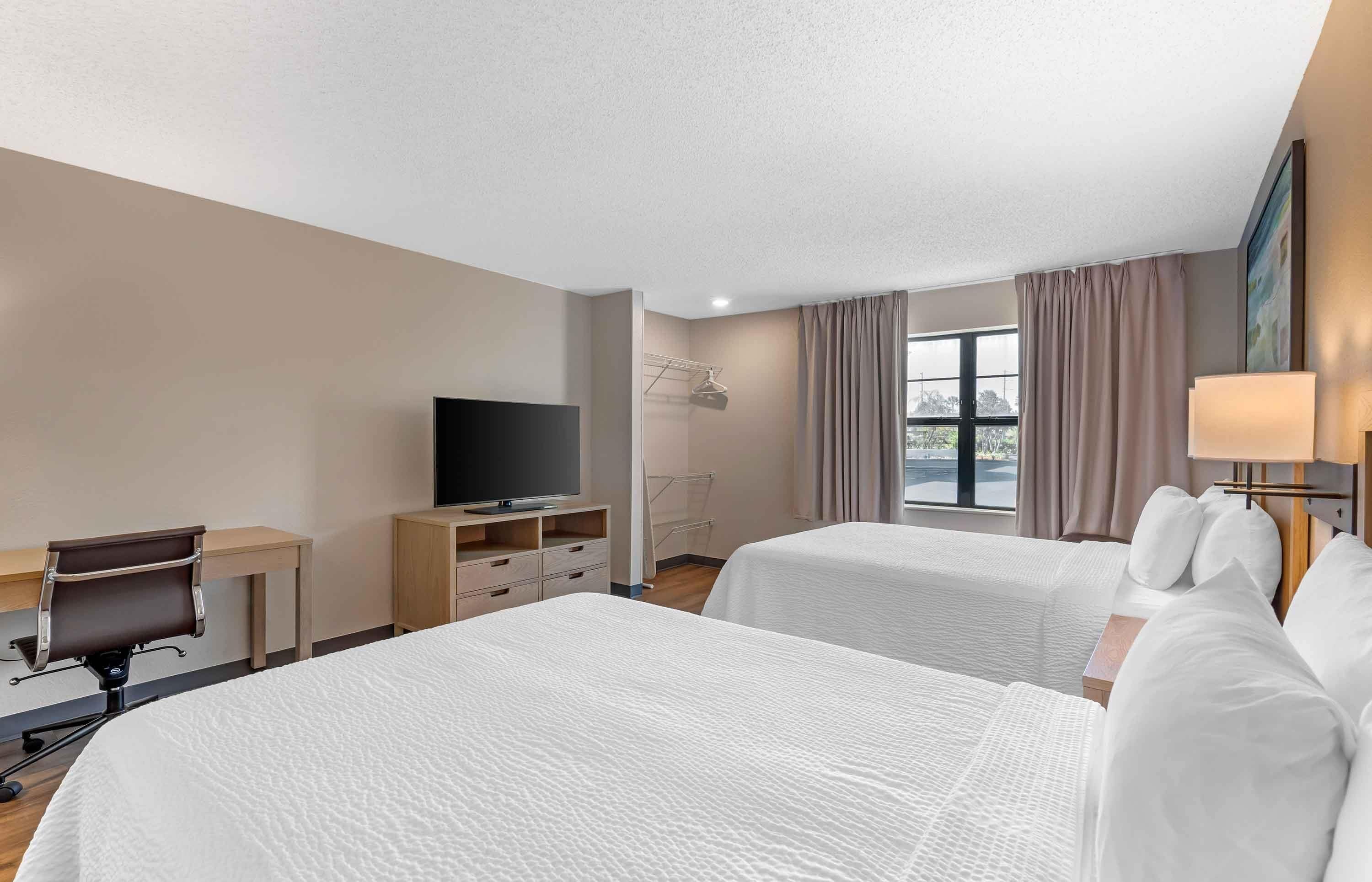 Una habitación de hotel con dos camas, un escritorio con una silla, un televisor y una ventana con cortinas.