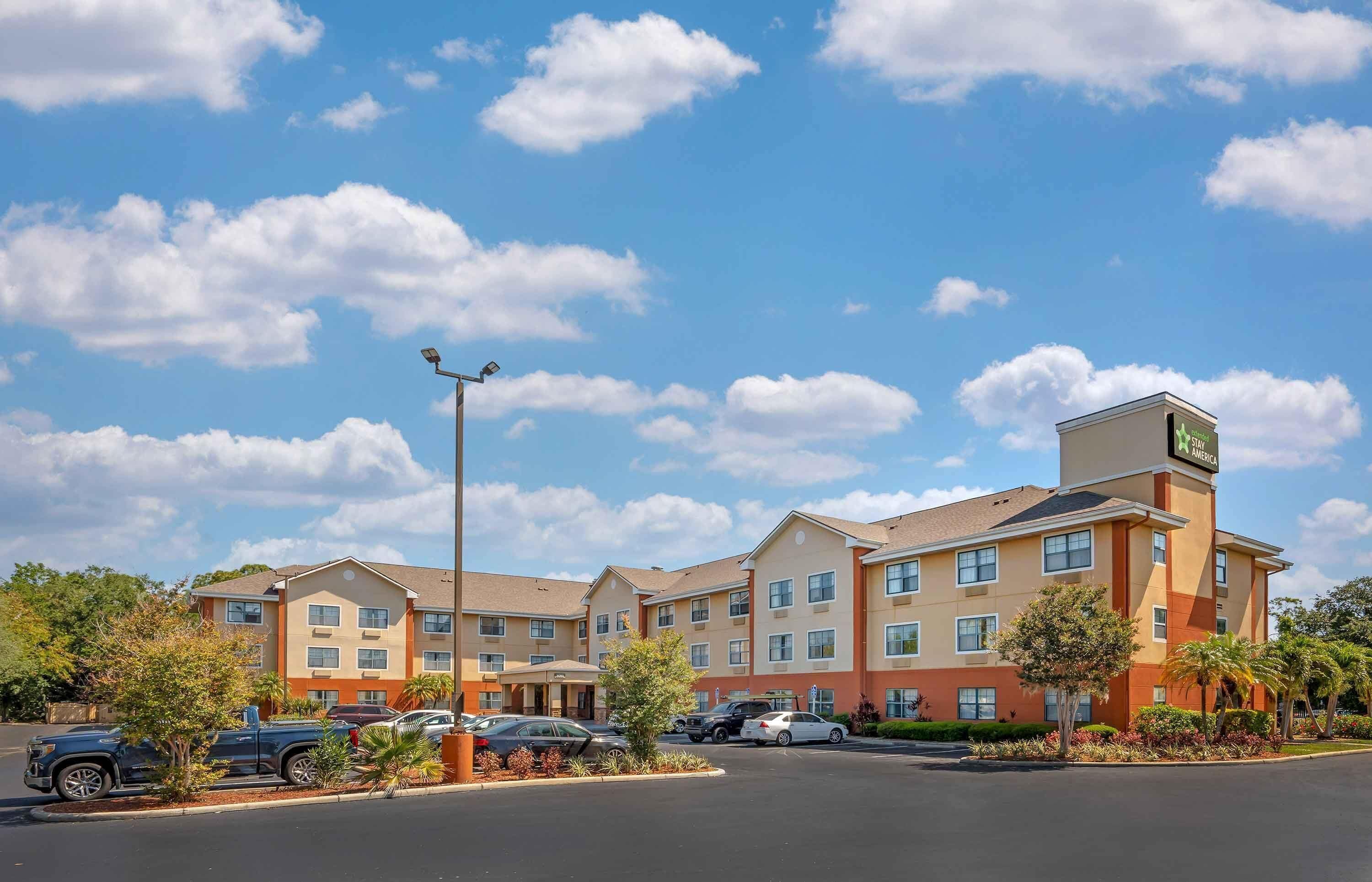 A multi-story hotel with a central courtyard, a parking lot, and a clear sky.