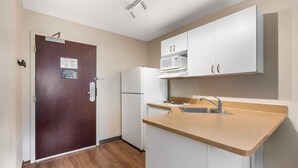 A compact kitchen with white cabinets, a microwave, a refrigerator, and a sink. - Extended Stay America Suites St Petersburg Clearwater ExecDr (Clearwater)