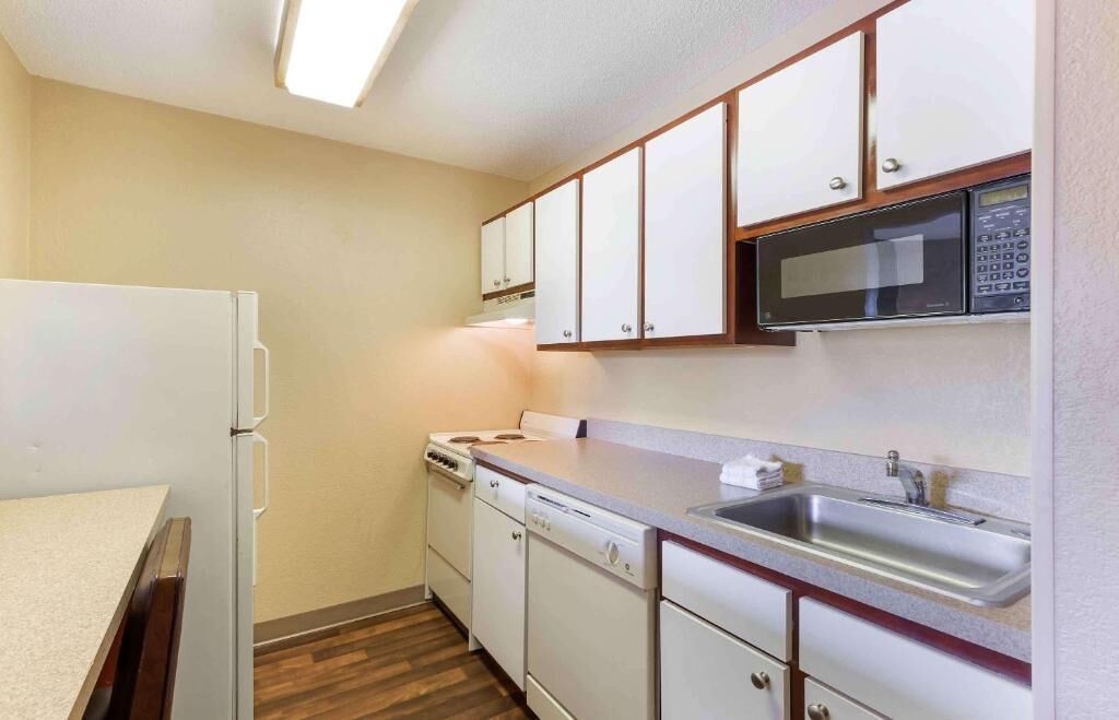 Una cocina compacta con armarios blancos, microondas, fregadero, estufa y lavavajillas.