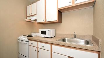Una cocina compacta con armarios blancos, estufa, microondas y pileta.