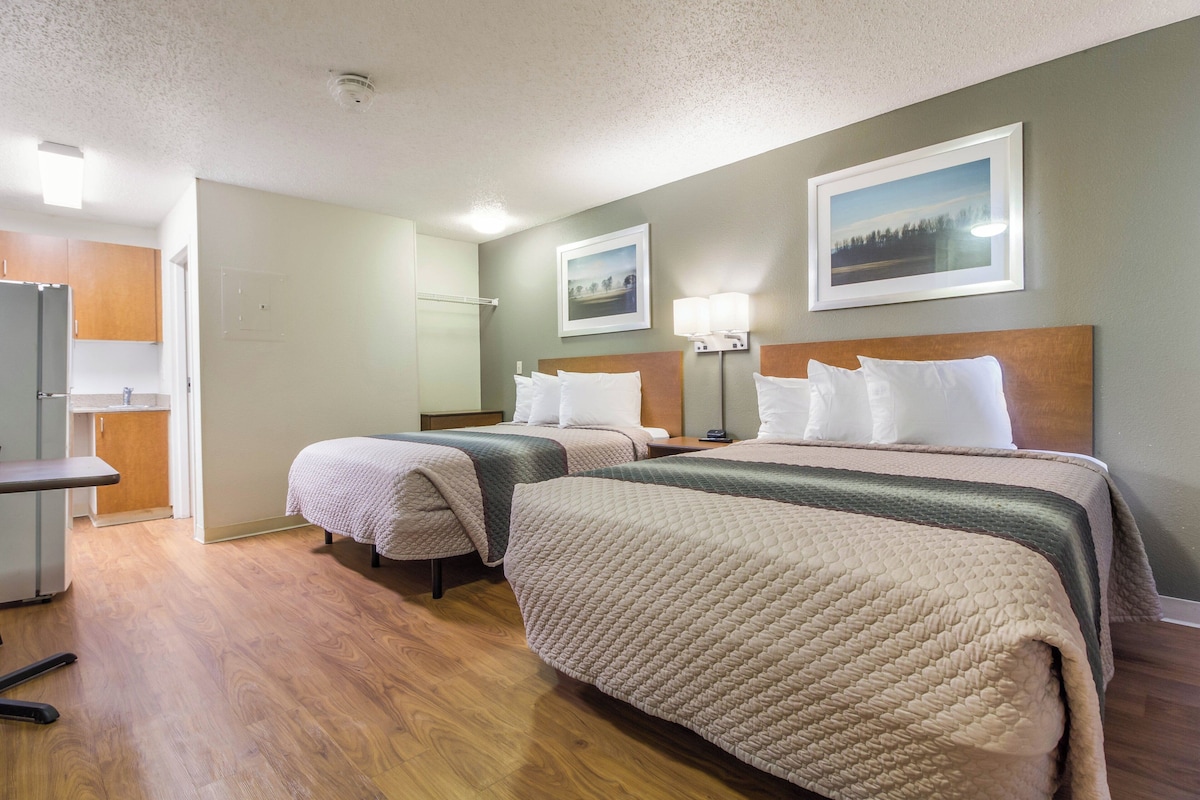 A hotel room with two beds, a desk, and a kitchenette.