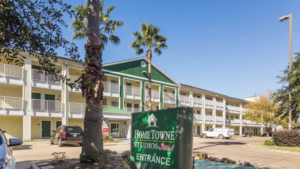 A multi-story building with a green entrance sign for Home Towe Studios by Red Roof. - HomeTowne Studios by Red Roof Houston - Northwest (Houston)