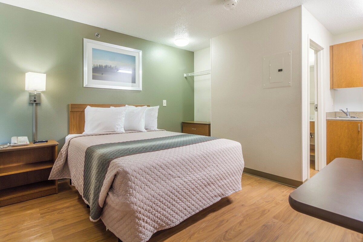 Ein Hotelzimmer mit Bett, Nachttisch, Lampe und einem Bild an der Wand.