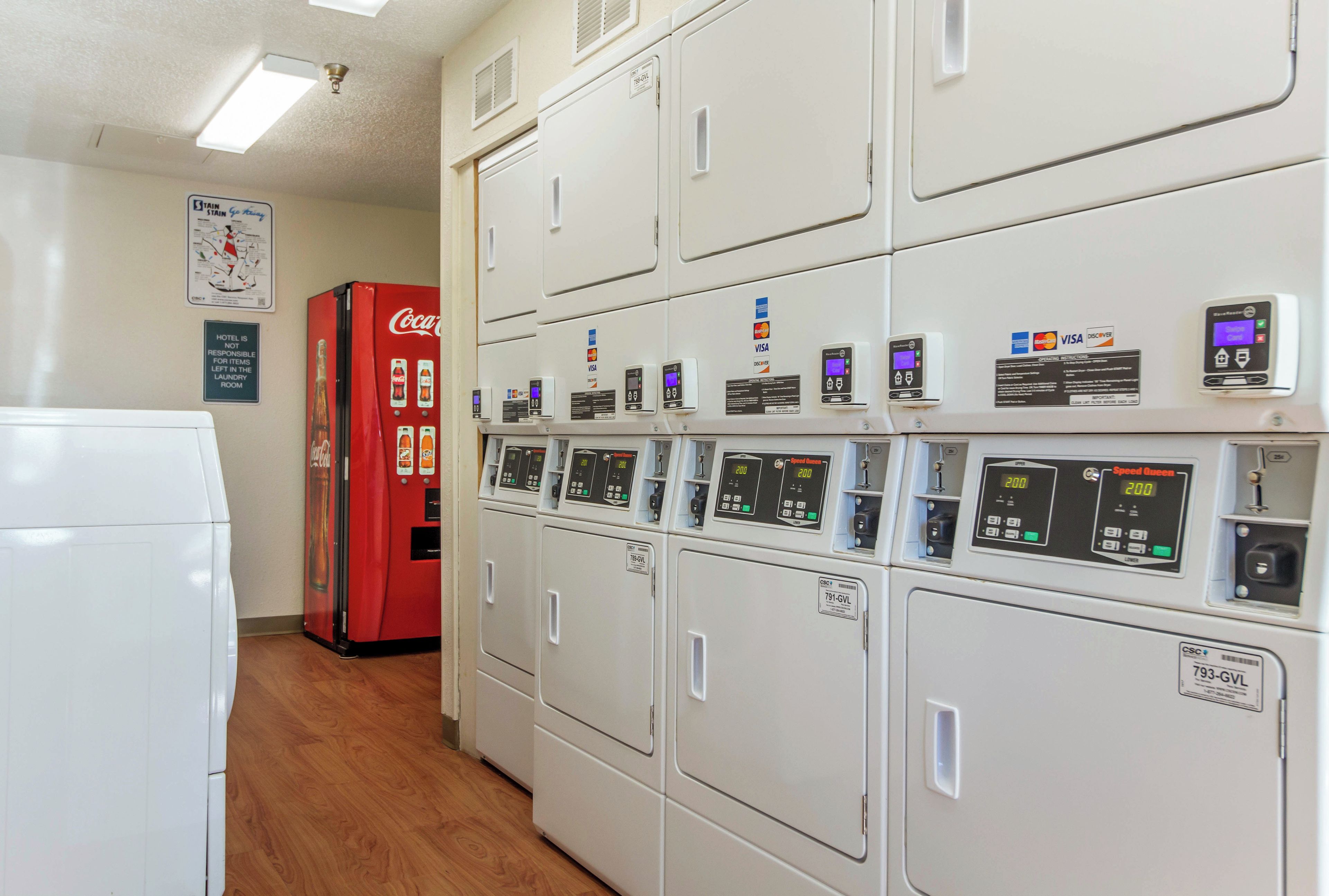A laundry room with multiple washing machines, a Coca-Cola refrigerator, and payment card machines.