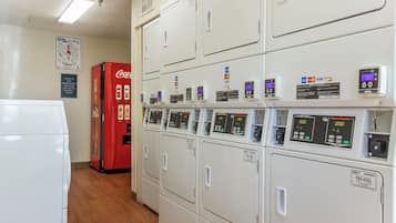 A laundry room with multiple washing machines, a Coca-Cola refrigerator, and payment card machines.